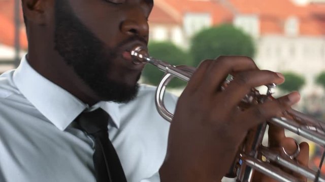 Black man playing trumpet. Musician on street background.