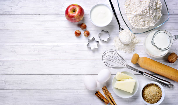 Baking ingredients: flour, eggs, milk, butter, brown sugar, cinnamon, nuts, yogurt, walnut and apple with eggbeater, cake pans and rolling pin. Top view, space for text.