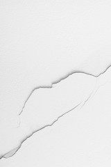 Crack on a white wall. Plaster crumbles from the ceiling. A long line is located on the textured surface throughout the length of the frame.