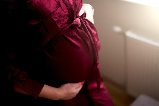 Pregnant woman in maxi dress holding hands on belly.