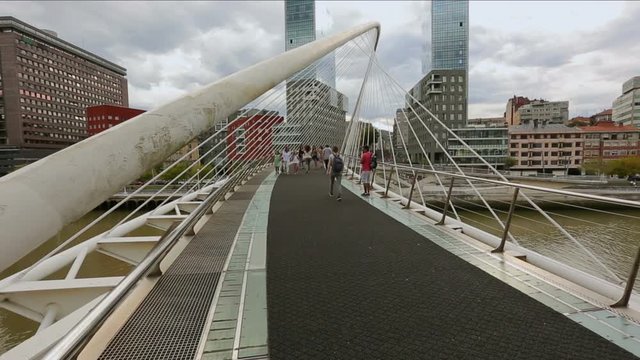 Pedestrians strolling across Zubizuri bridge over Nervion river in Bilbao, Spain