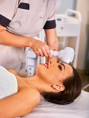Obraz na płótnie Canvas Ultrasonic facial treatment on ultrasound face machine. Woman receiving electric lift massage at spa salon. Electronic stimulation female muscles. Professional equipment microcurrent therapy .