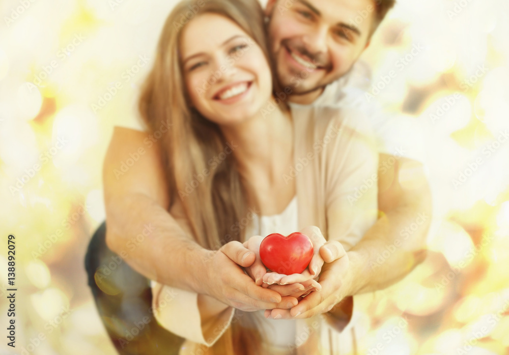 Poster young couple holding small red heart, on light background