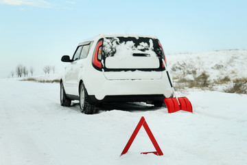 Car stuck in snowdrift and emergency stop sign on winter road