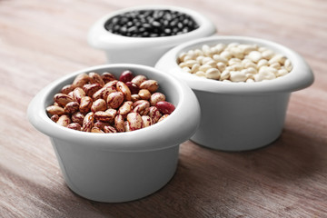 Assortment of haricot beans in bowls on wooden table, closeup