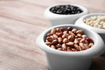 Assortment of haricot beans in bowls on wooden table, closeup