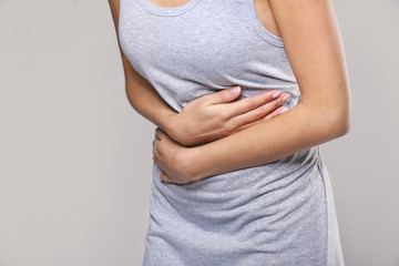 Close up view of woman suffering from abdominal pain on grey background. Gynecology concept