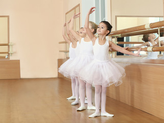 Fototapeta premium Group of little ballerinas practicing ballet using bar at class