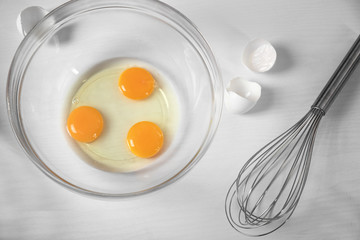 Cracked eggs in a glass bowl on kitchen table