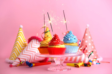 Cupcakes with sparklers on color background