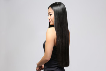 Beautiful Asian woman with long straight hair on light background