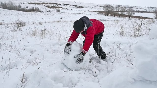 Teen boy rolling a ball of winter snow to build a fortress. sculpts snowman snow