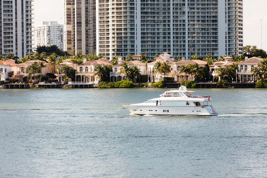 Luxury yacht moves past a row of expensive homes in a tropical setting