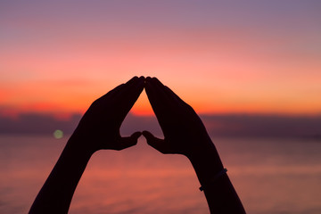 Heart shape with hands at sunset background