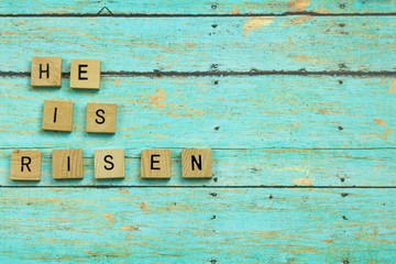 He is Risen Christian blocks on a blue wood plank background