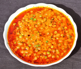 Indian style muttar masala Sabji (spicy green pea vegetable) in white bowl on black background.