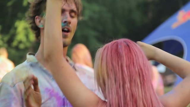 Happy man kissing girlfriend at Holi festival, couple dancing at open-air party