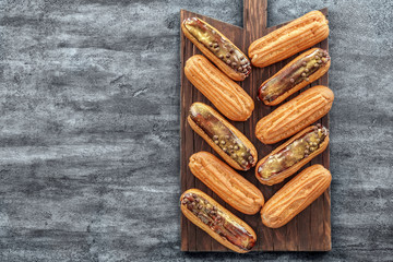 Delicious eclairs on wooden cutting board, top view