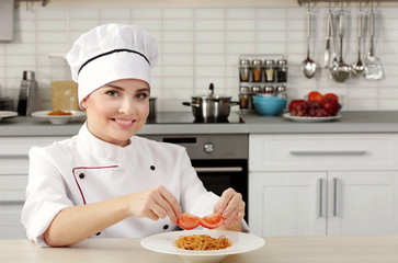 Young woman chef putting tomato slices on plate with pasta