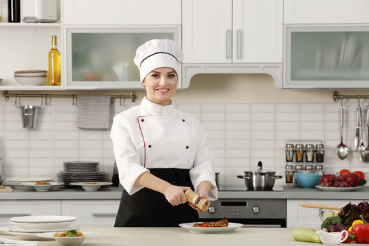 Young woman chef adding pepper to meat dish on plate