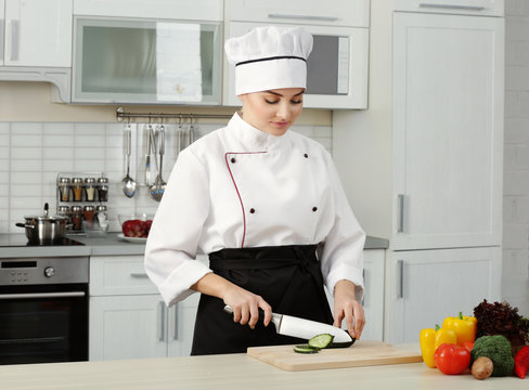 Young woman chef cutting cucumber in modern kitchen