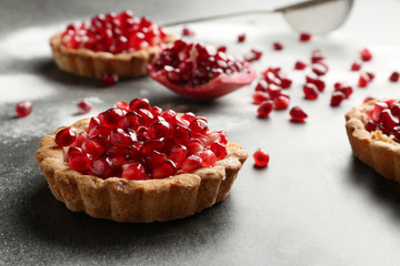 Tasty tarts with fresh seeds of pomegranates on gray table