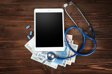 Tablet, stethoscope and money on wooden background. Medical concept