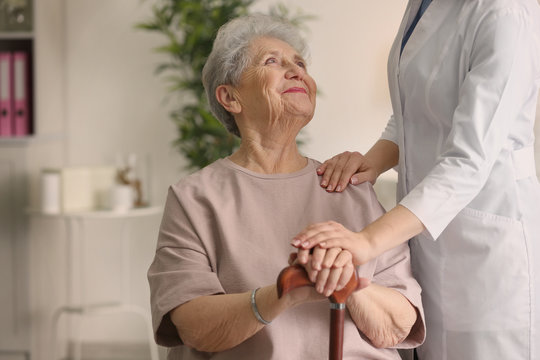 Elderly Woman Holding Hands On Walking Stick And Listening Doctor In Light Room