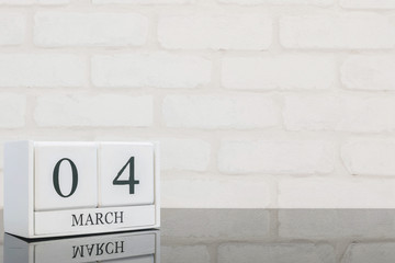 Closeup white wooden calendar with black 4 march word on black glass table and white brick wall textured background with copy space , selective focus at the calendar