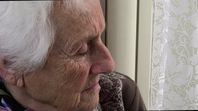 Profile of depressed old woman alone looking out the window