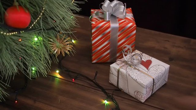 The man puts gift boxes under the Christmas tree. Fir stand on the wooden table, decorated glowing garland and Christmas toys. Boxes with gift wrapped in a colored paper and tied with festive ribbon