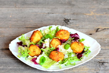 Fried mashed potato balls on a plate isolated on vintage wooden background. Fried potato balls with pumpkin seeds served with fresh salad mix and basil. Closeup