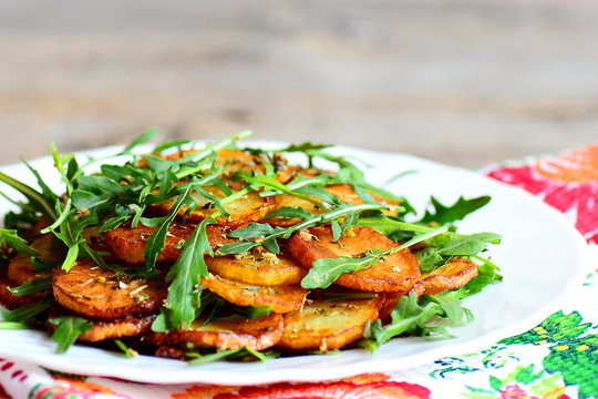 Golden potatoes with arugula on a plate. Round roasted potatoes with fresh arugula and condiments. Fast and tasty potato recipe. Closeup