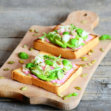 Sandwiches with avocado, lettuce, basil, pumpkin seeds and creamy pink beet sauce. Vegetarian sandwiches on a wooden board. Healthy lunch idea. Closeup