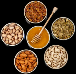 Pistachios, almonds, peanuts, pumpkin seeds, raisins and honey in ceramic plates.