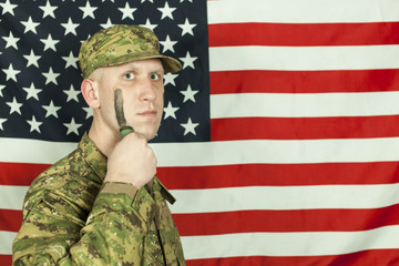 Soldier with camouflage paint on cheek against of  American flag. Portrait