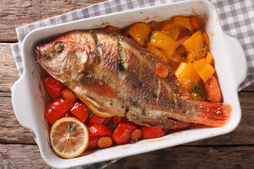 Tilapia baked with vegetables and thyme close up in baking dish. Horizontal top view