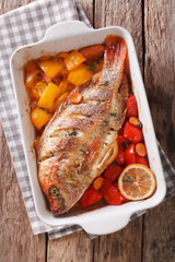 Tilapia fish baked with bell peppers, carrots and thyme close up in baking dish. vertical top view