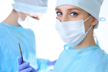 Close up of surgeon woman looking at camera while colleagues performing in background in operation...