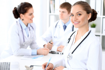 Happy female doctor and medical staff discussing something while sitting at the table.  Successful team at health care and medicine concept