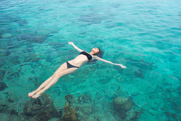 Beautiful young brunette woman in black swimsuit swims into clear azure water of caribbean sea