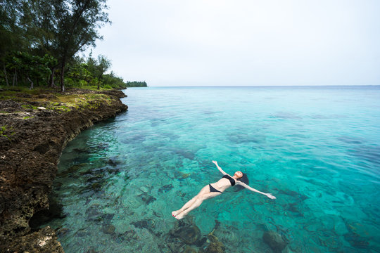 Beautiful young brunette woman in black bikini swimsuit is swimming into clear azure water of caribbean sea