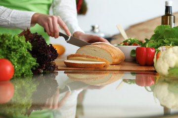 Closeup of human hands slicing bread in kitchen on the glass table with reflection. Healthy meal and vegetarian concept