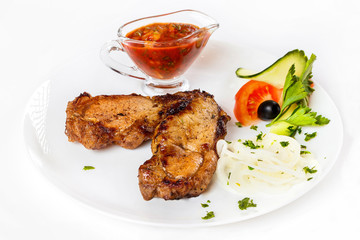 Grilled pork shashlik with red spicy sauce and vegetables on plate isolated  at white background.