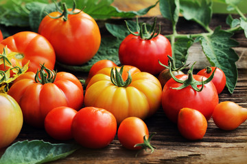 Red tomatoes with leaves on wooden background.