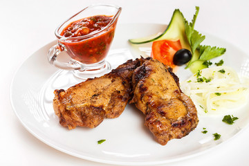 Grilled pork shashlik with red spicy sauce and vegetables on plate isolated  at white background.