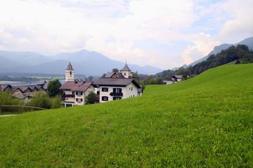 Fototapeta na wymiar Travel to Sankt-Wolfgang, Austria. The green meadow with the houses in the mountains.