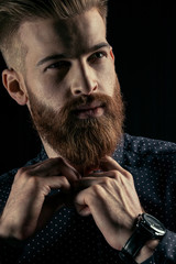 Close-up portrait of handsome bearded man hipster buttoning shirt