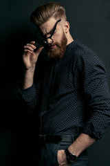 Handsome bearded young man hipster with hand in pocket holding eyeglasses