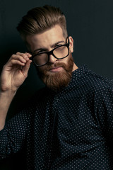 Obraz premium Handsome bearded young man hipster adjusting eyeglasses and looking at camera